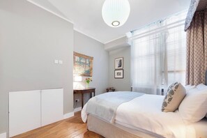A bedroom with a bed, a bedside table, a lamp, and a window with curtains.