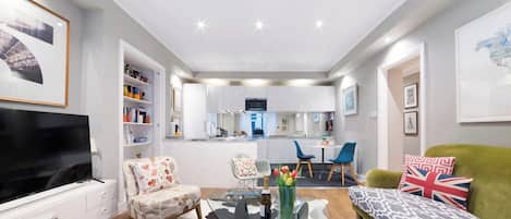 A modern living room with a flat-screen TV, a sofa, a glass coffee table, and a dining area with chairs.