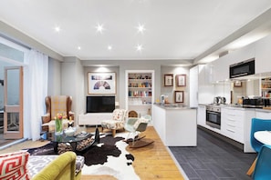 Ein modernes Wohnzimmer mit Sofa, Sessel und Couchtisch, eine Küche mit Geräten und ein Essbereich, sowie ein großes Fenster.