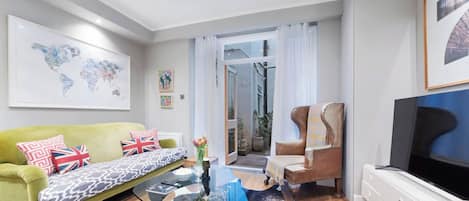 A modern living room with a green sofa, a glass coffee table, a leather armchair, and a flat-screen TV.