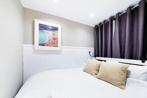 A bedroom with a bed, a headboard, a framed picture on the wall, and a window with curtains.