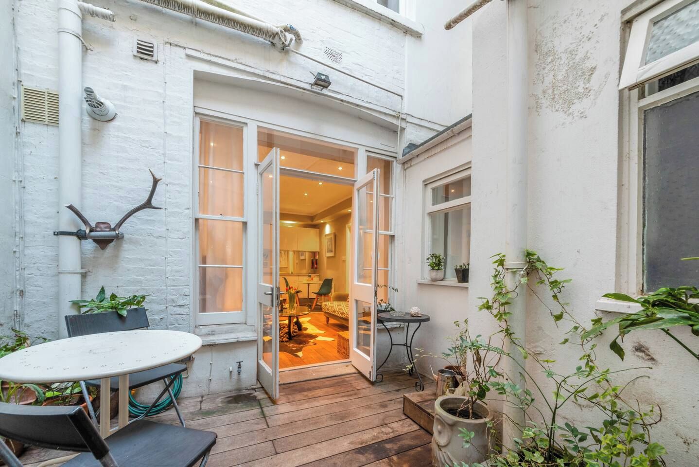 A small patio area with a table and chairs, a wooden deck, and potted plants.