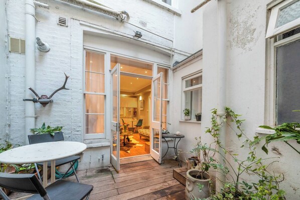 A small patio area with a table and chairs, a wooden deck, and potted plants.