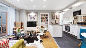 Ein modernes Wohnzimmer mit einer Couch, einem Couchtisch und einem Fernseher. Es gibt eine Küchenzeile mit einer Mikrowelle, einem Herd und Schränken.
