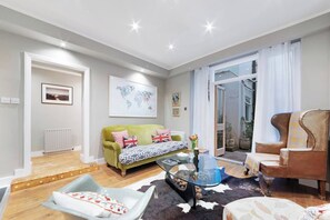 A living room with a green sofa, a glass coffee table, and a leather armchair.
