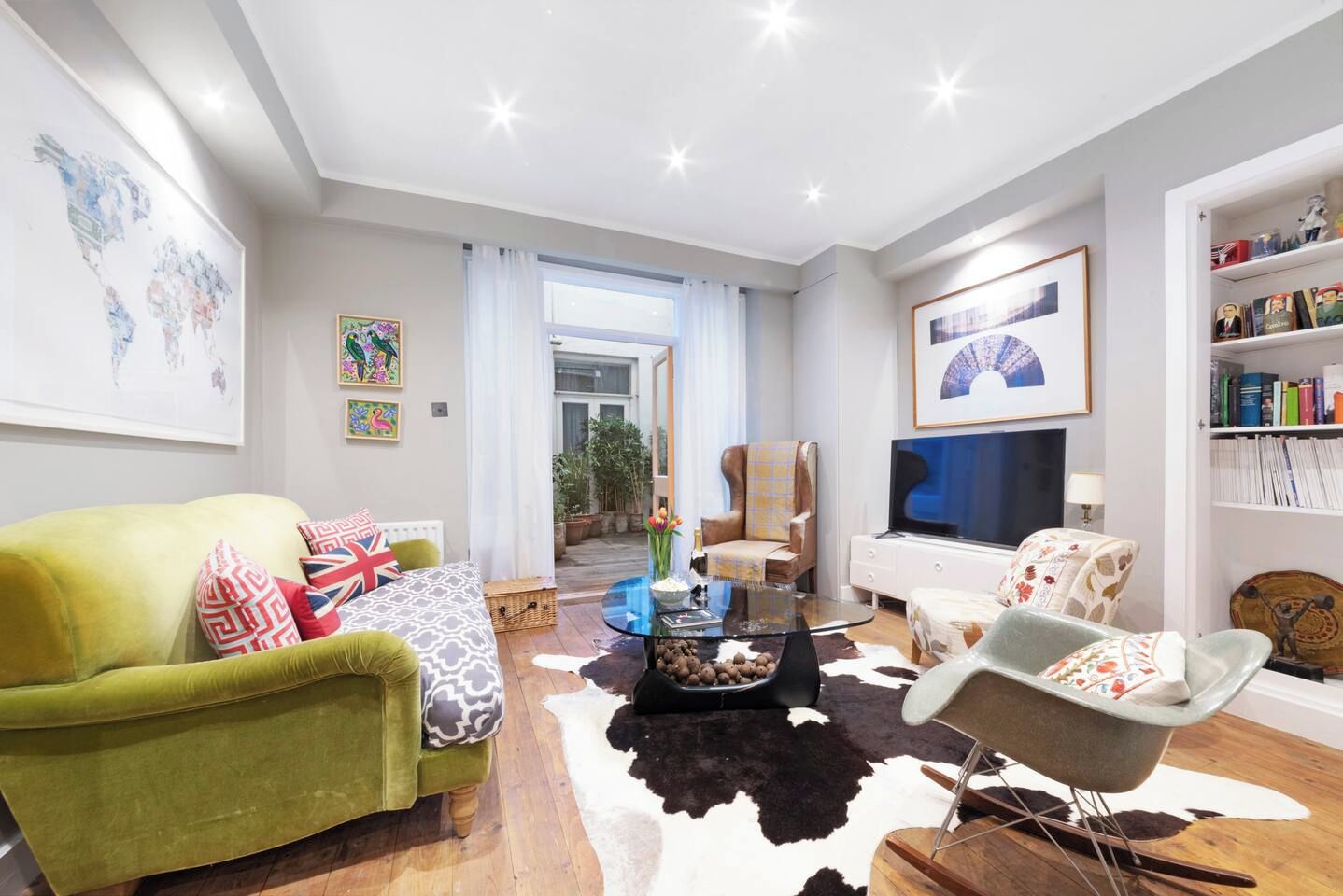 Una sala de estar moderna con un sofá verde, una mesa de centro de vidrio y un tapete de cuero de vaca.