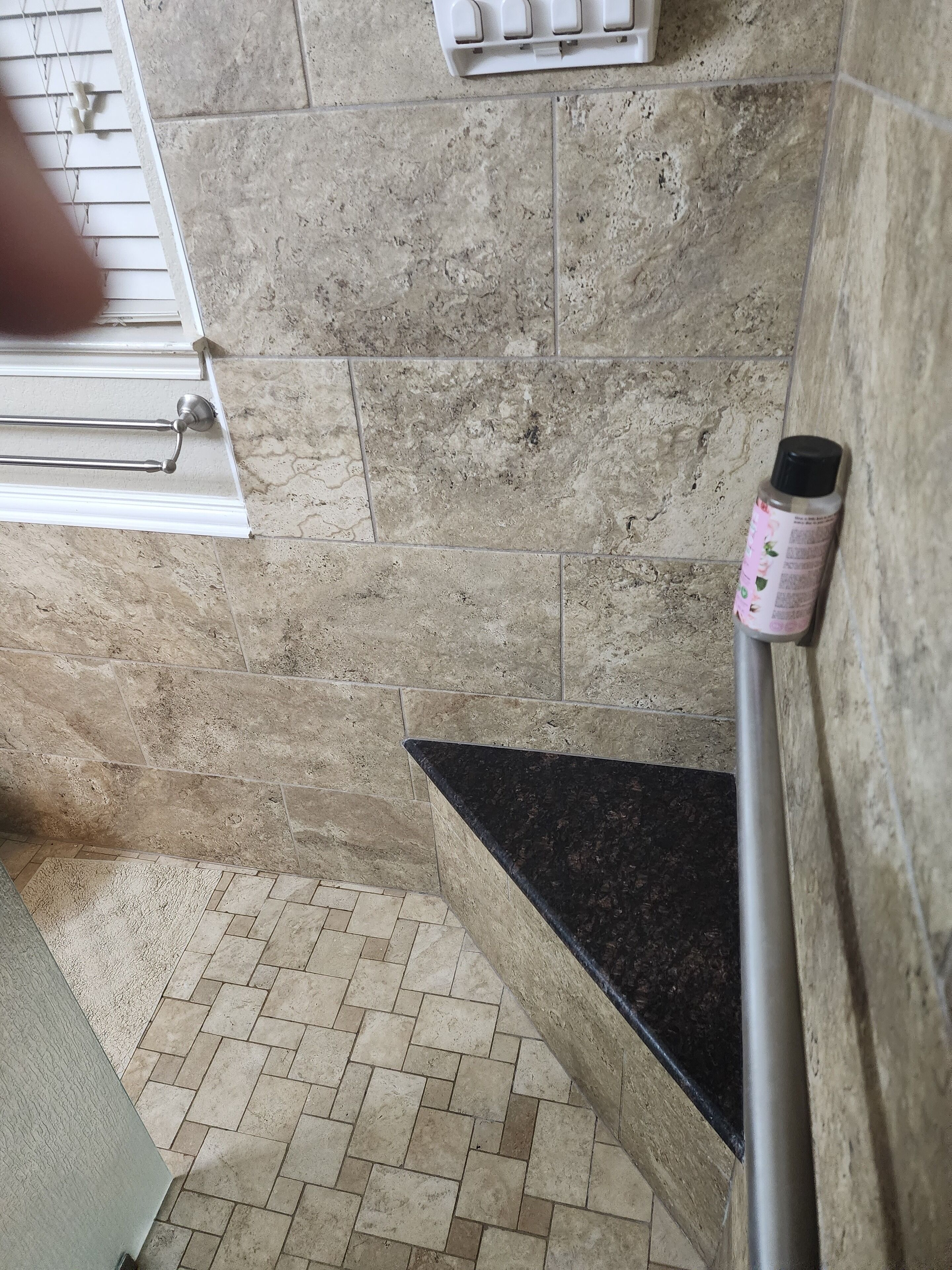 A bathroom with beige tiles, a black countertop, and a hand dryer.