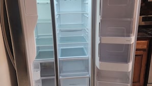 An open refrigerator with multiple shelves and a pull-out drawer, situated in a kitchen with wooden cabinets and a tiled floor. - Texas Motor Speedway Comfort Zone (Justin)