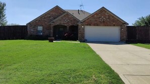 A two-story brick house with a garage, a front lawn, and a wooden fence. - Texas Motor Speedway Comfort Zone (Justin)