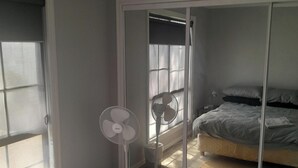 A bedroom with a bed, a standing fan, a sliding glass door, and a window. - SizzlingSummerRates@TheWhiteHouse (Carrum Downs)