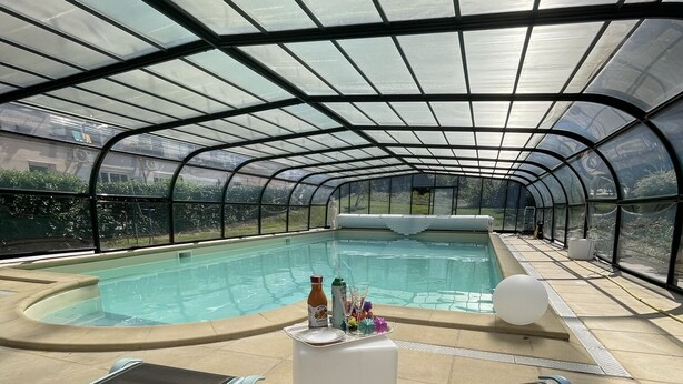 A covered swimming pool with lounge chairs and a small table with drinks.