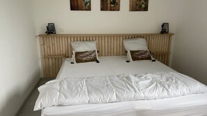A neatly made bed with white bedding and two decorative pillows, a wooden headboard, and three wall-mounted leaf art pieces.