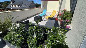 A rooftop terrace with two lounge chairs, a small table, and potted plants.