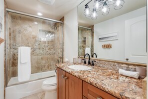 Uma casa de banho moderna com chuveiro envidraçado, banheira branca e lavatório com bancada de granito.