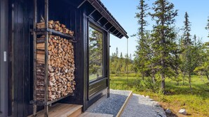 A cabin with a stack of firewood against the wall, a wooden deck, and a view of a forested landscape. - 3 bedroom amazing home in Tuddal (Tuddal)