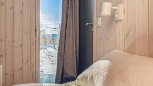 A bedroom with wooden walls, a bed with a white duvet, a window with a view of a snowy landscape, and a wall-mounted light fixture. - 3 bedroom amazing home in Tuddal (Tuddal)