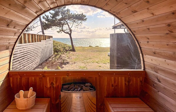 A wooden sauna with a view of the sea, a wooden bench, and a container labeled 'HARVIA'. - Awesome home in Martofte with sauna (Martofte)