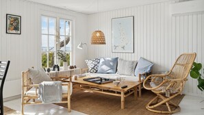 A cozy living room with a wooden coffee table, wicker chairs, a sofa with patterned cushions, and a large window with a view of the outdoors. - Awesome home in Martofte with sauna (Martofte)