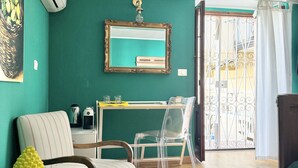 Sala de estar com paredes verde-turquesa, piso de madeira, uma escrivaninha com computador, uma cadeira, um sofá e uma mesa de jantar.