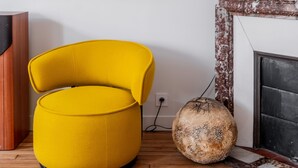 Una habitació amb una cadira groga, una llar de foc i una obra d'art emmarcada a la paret.