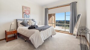 Une chambre à coucher comprenant un lit, une table de chevet, un bureau, une grande fenêtre et une vue sur le paysage.
