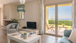 Una sala de estar con televisor, sofá y mesa de centro, chimenea y vista al mar a través de amplios ventanales corredizos.