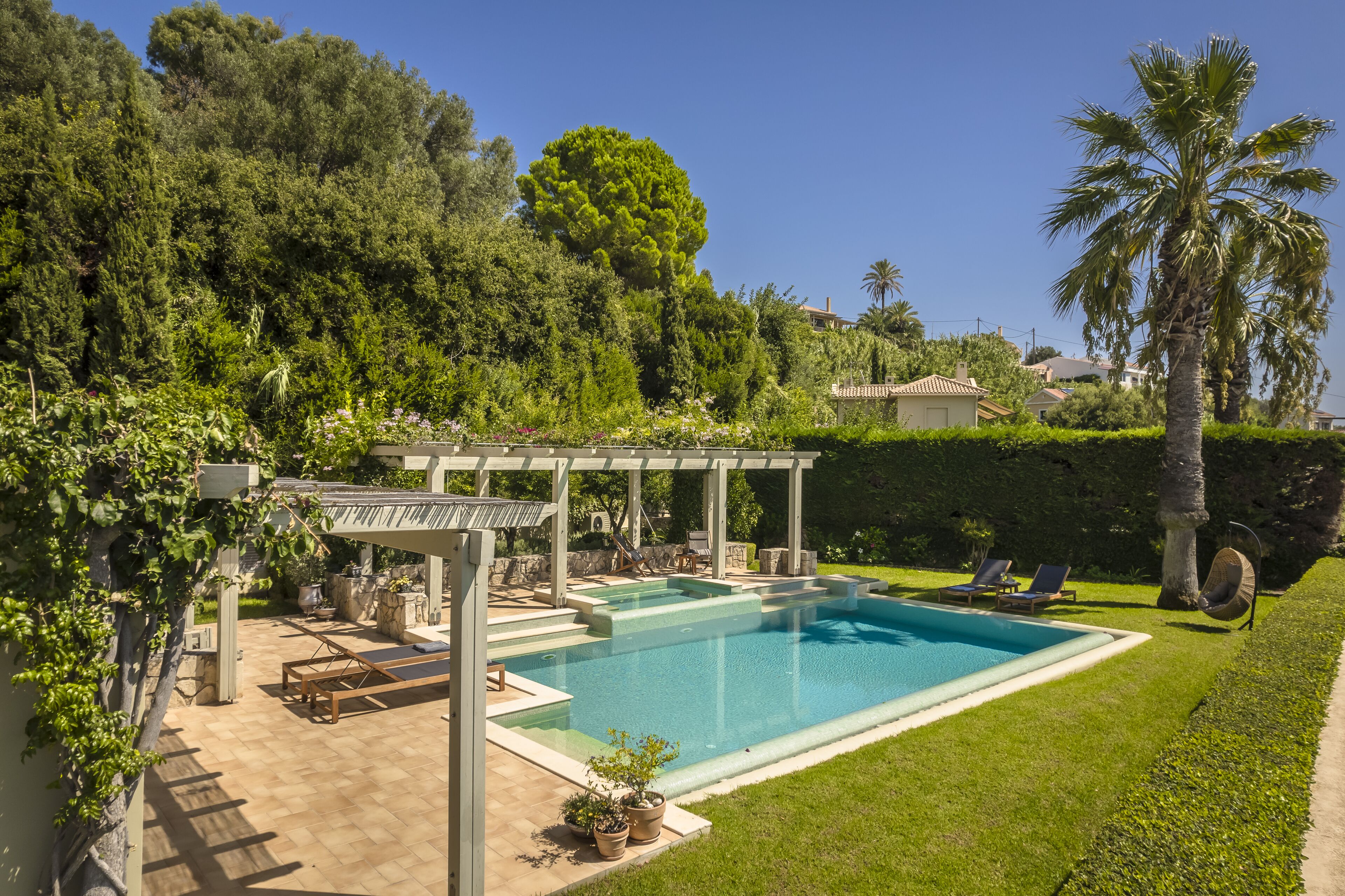 A swimming pool with a pergola, lounge chairs, and a garden area with potted plants.