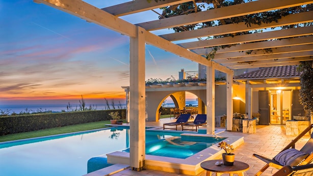 Zona de piscina con vistas al atardecer, sillas de descanso y una pérgola.