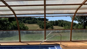 Une piscine intérieure dotée d’une terrasse en bois et offrant une vue sur un paysage verdoyant, visible depuis un espace abrité.