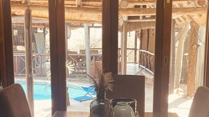 A wooden dining table with two glass bottles and a vase, set against a backdrop of a wooden deck and a pool area. - Nyala Luxury Safari Tents (Nkomazi)