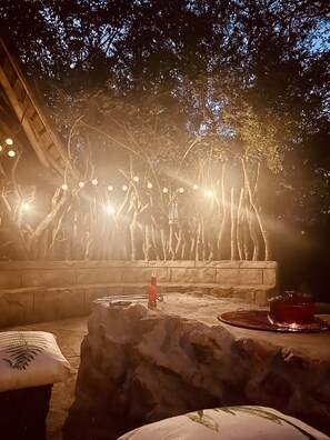 An outdoor seating area with stone walls, string lights, and a fire pit.