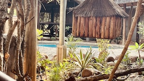 A rustic outdoor area with a thatched-roof structure, a wooden fence, and a pool. - Nyala Luxury Safari Tents (Nkomazi)