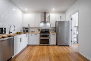 A modern kitchen with white cabinets, stainless steel appliances, and wooden flooring. - Harmony at The Key | 2 Kitchens • Near UF & DT (Gainesville)