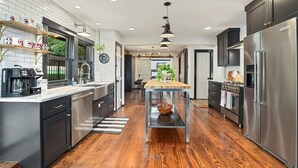 A modern kitchen with dark cabinetry, stainless steel appliances, and a central island. - Retro Razorback - Pickleball-Golf-Spa-UofA (Fayetteville)