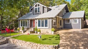 A two-story house with a stone foundation, a large front porch, and a well-maintained lawn. - Retro Razorback - Pickleball-Golf-Spa-UofA (Fayetteville)