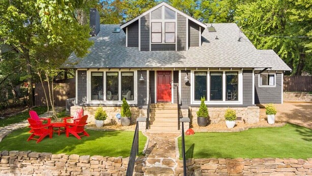 A two-story house with a stone foundation, a red front door, and a covered porch with potted plants. - Retro Razorback - Pickleball-Golf-Spa-UofA (Fayetteville)