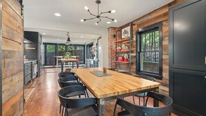A modern kitchen with a wooden table and chairs, a brick accent wall, and a large window. - Retro Razorback - Pickleball-Golf-Spa-UofA (Fayetteville)