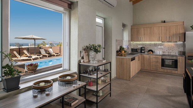 A modern kitchen with wooden cabinets, a built-in oven, and a large window overlooking a pool area. - Roxanne Luxury Villa, Private Pool & Seaview (Chania)