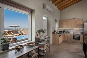 A modern kitchen with wooden cabinets, a built-in oven, and a large window overlooking a pool area. - Roxanne Luxury Villa, Private Pool & Seaview (Chania)