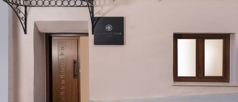 L’entrée d’un hôtel, avec une porte en bois, une enseigne noire portant un logo et une fenêtre avec des stores.