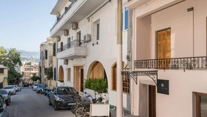 Eine schmale Straße, gesäumt von mehrstöckigen Gebäuden, parkenden Autos und einem Motorrad.