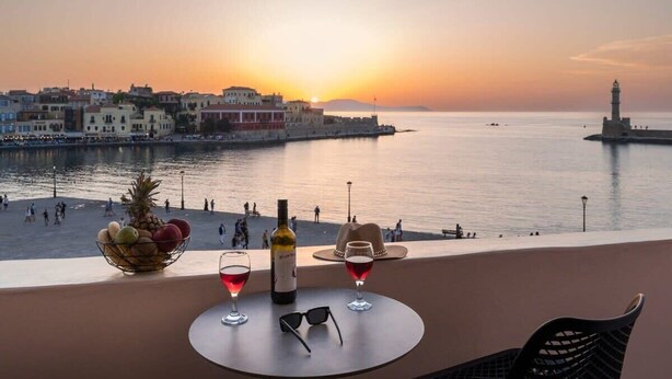 Sonnenuntergangblick von einem Balkon mit gedecktem Tisch für zwei Personen, inklusive Weinflasche, Gläsern, Obstschale und Hut.