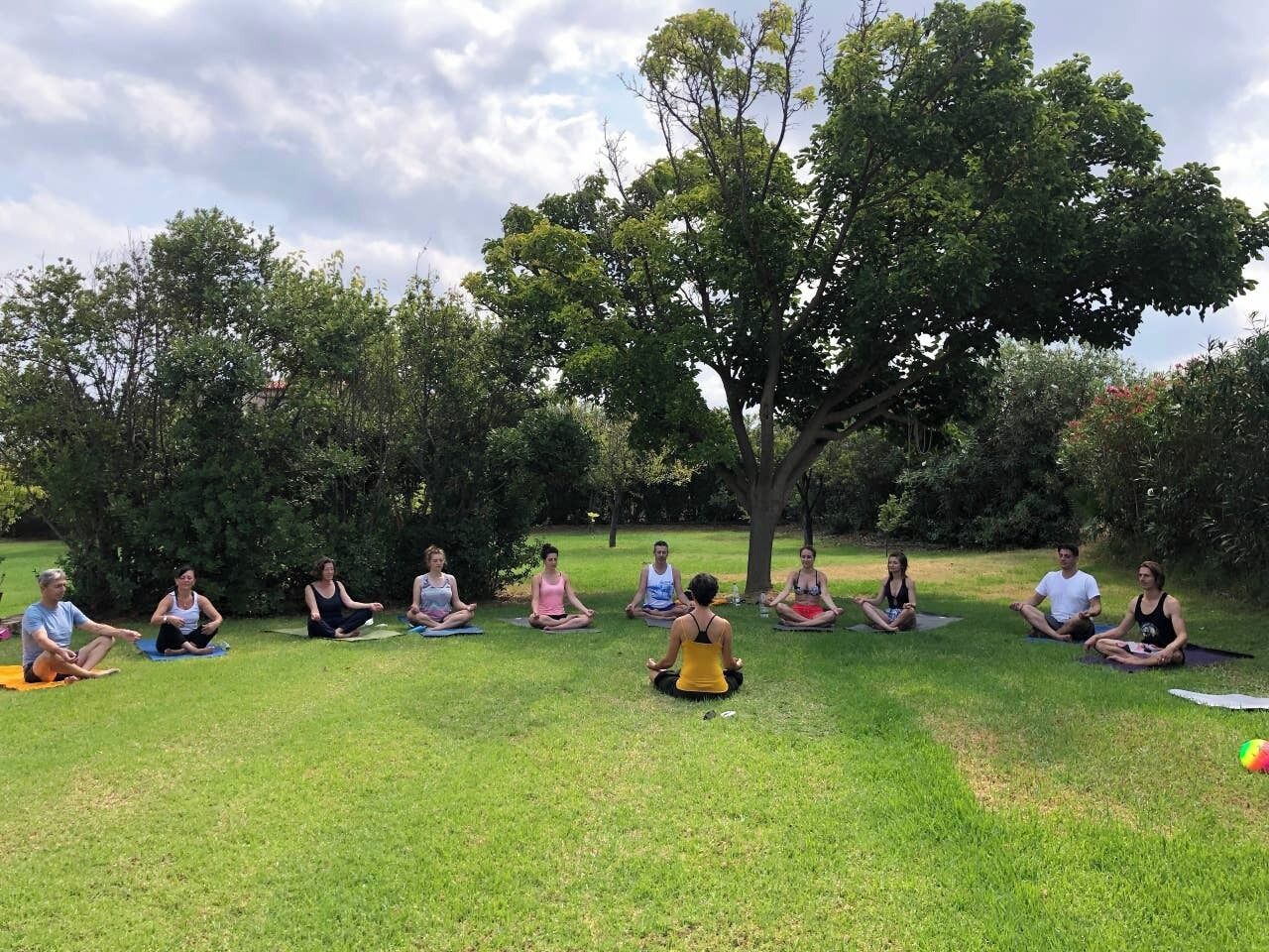 A group of people sitting in a circle on the grass outdoors, likely engaged in a group activity or class.