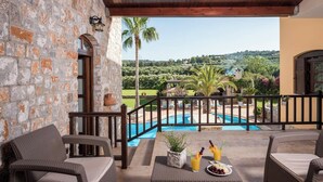 A stone-walled balcony with wicker furniture, a pool, and a view of a lush landscape. - Natali Luxury Villa (Iason Villas), 9 Bedrooms (Chania)