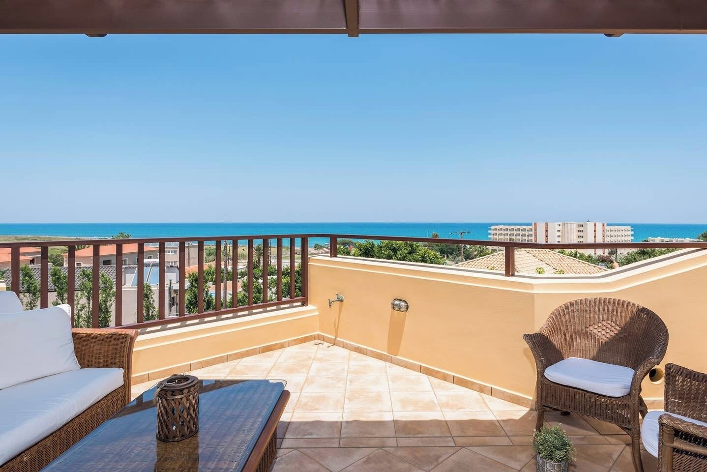 Un balcon agrémenté de meubles en osier, avec vue sur la mer et des bâtiments en arrière-plan.