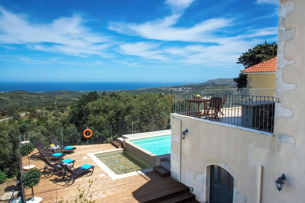 A pool area with a view of the sea, surrounded by a wooden deck and lounge chairs.