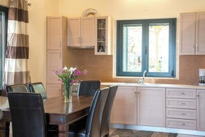 A kitchen with a dining table, chairs, a vase of flowers, and a window with shutters. - Villa Cretan View with Heated Swimming Pool (Patima)