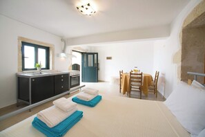 A compact room with a kitchenette, a dining area with a table and chairs, and a bed with folded towels. - Villa Cretan View with Heated Swimming Pool (Patima)