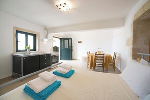 Een slaapkamer met een bed, nachtkastje, bureau met stoel, raam en een kitchenette.