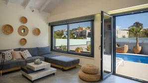 Ein modernes Wohnzimmer mit einem grauen Sofa, einem Couchtisch und einem großen Fenster mit Blick auf einen Pool und Gebäude.
